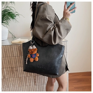 Detail of black faux leather tote with litchi texture and cute brown bear pendant