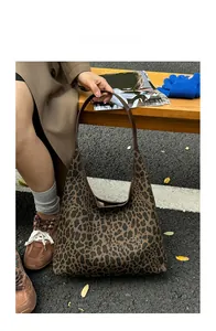 Fashionable leopard print tote bag with brown leather straps displayed on a wooden bench