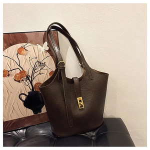 Classic dark brown leather tote bag with gold buckle hardware on a vintage leather bench