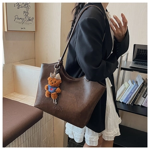 Detailed texture of brown faux leather tote bag with a cute plush bear charm accessory