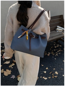 Blue tote bag with brown leather strap and wooden bead charm in an autumn setting