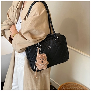 Close-up of black quilted tote bag with brown plush bear charm worn by a model