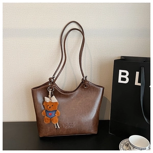 Macro detail of dark brown retro leather tote bag featuring a cute teddy bear charm