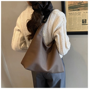 Detail of a minimalist dark brown matte leather tote bag worn by a model in a retro setting