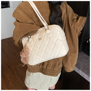 Detail view of cream quilted leather tote bag with brown plush bear charm accessory