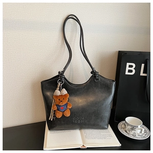 Close-up of black matte tote bag with plush bear charm and embossed logo detail
