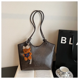 Detail of dark brown leather tote bag featuring a cute teddy bear charm and logo embossing