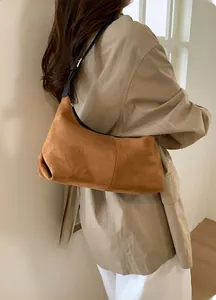 Brown suede dumpling bag shown on shoulder with adjustable strap and metallic hardware