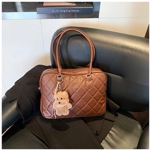 Detail of brown quilted tote bag with metallic logo and cute plush bear charm