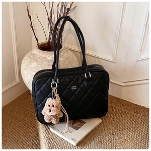 Detail of black quilted tote bag with a cute bear charm and soft ribbon on a shoulder strap