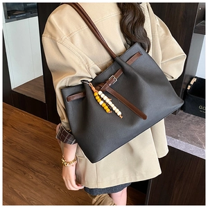 Detail of grey leather tote bag featuring brown straps and a decorative beaded tassel
