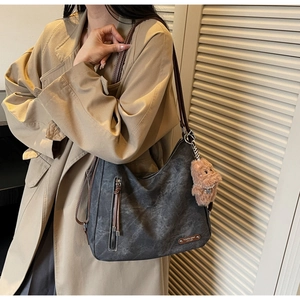 Chic grey canvas hobo bag with leather straps and bear charm shown on a model