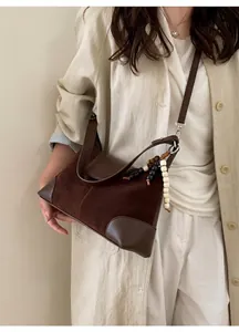 Détail d'un sac bandoulière en daim marron avec finitions en cuir et breloque en perles