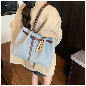Detail of light blue tote bag with brown straps and stylish beaded charm accessory