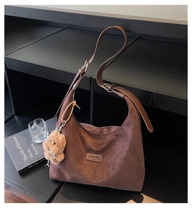 Brown suede hobo bag detail with plush bear charm and adjustable shoulder strap