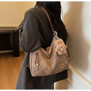 Brown frosted leather tote bag with plush bear charm worn over a gray blazer