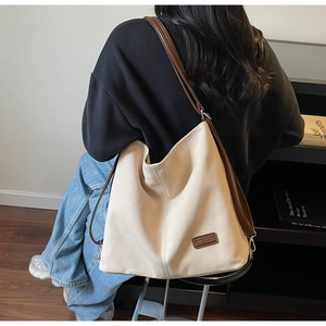 Detail view of cream canvas tote bag featuring premium leather straps and logo patch