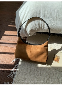 Detailed texture of brown suede hobo bag with sleek black leather strap on white rug