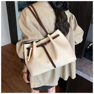 Detail shot of a large beige canvas tote bag with brown leather straps and wooden beads