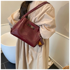 Detail of burgundy patent leather handbag with gold studs and triangular charm accessory