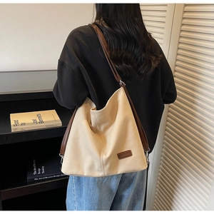 Detail of cream canvas tote bag featuring brown leather trim and shoulder straps on a model