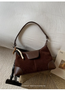 Detailed shot of retro brown suede patchwork handbag with decorative bead tassel on straw chair