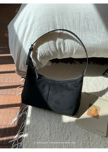 Minimalist black faux suede half-moon shoulder bag with zipper on a plush carpet
