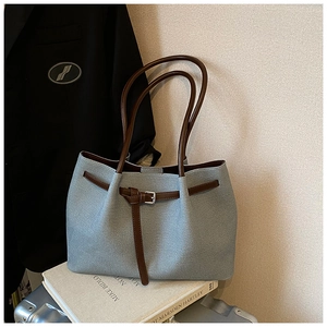 Detail of grey-blue tote bag with brown straps and silver buckles on minimalist background
