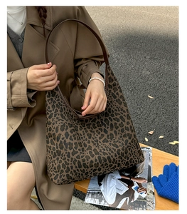 Close-up of a large leopard print canvas hobo bag with brown leather strap detail