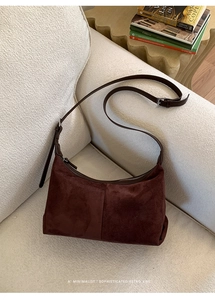 Detail of burgundy suede shoulder bag with brown leather strap on a minimalist sofa