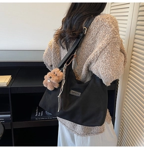 Detail of black canvas Hobo tote bag with plush dog charm and leather logo on strap