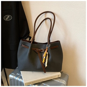 Detail view of dark grey leather tote bag with brown straps and wooden bead charm on suitcase