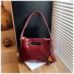 Detail of burgundy glossy pleated shoulder bag with mini pouch on a wooden surface