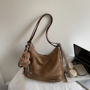 Brown hobo shoulder bag with a teddy bear charm shown next to a laptop on a white desk