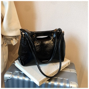 Detail of black glossy crinkled leather tote bag with gold rivets and cutout handle