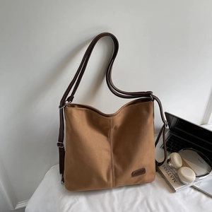 Detail of a brown canvas tote bag featuring an adjustable faux leather strap and logo patch