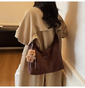 Close-up of brown suede tote bag with cute plush puppy charm and brand detail