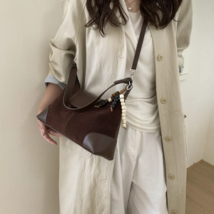 Detail of retro brown suede handbag with leather stitching and beaded shoulder strap