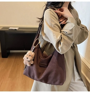 Detail of dark brown suede tote bag featuring a plush dog charm and brand logo