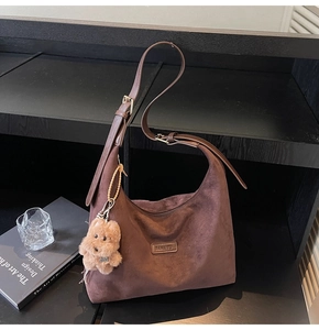 Detail of a large dark brown suede tote bag with brand plaque and cute puppy pendant
