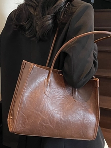 Retro oversized dark brown tote bag in pleated faux leather worn by a model in a suit