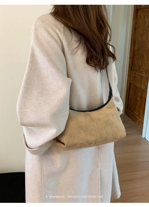 Minimalist beige suede hobo bag with black leather trim worn on shoulder over-the-back