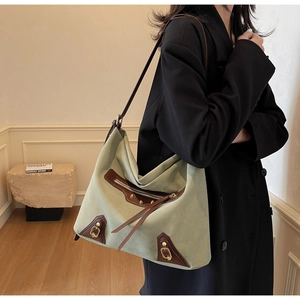 Detail view of sage green tote bag with brown leather trim and long tassel zippers