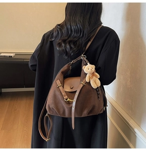 Details einer dunkelbraunen Wildleder-Schultertasche mit Goldschnallen und Bärenanhänger