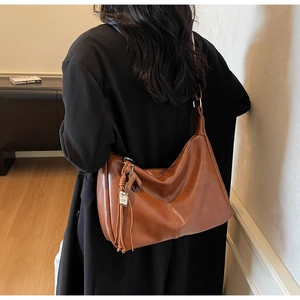 Vue détaillée du sac hobo en cuir marron avec pompon porté à l'épaule par une femme