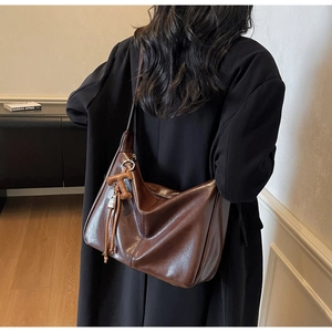 Détail du sac cabas marron vintage avec pompon en cuir et pendentif T à l'épaule