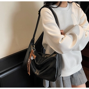 Détail d'un grand sac cabas noir en cuir avec gland marron et pendentif métallique chic