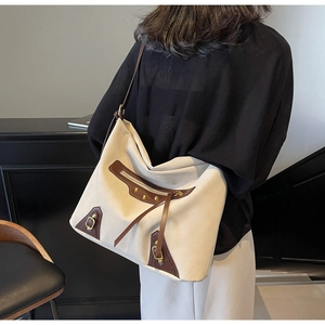Detail of vintage canvas tote bag with brown leather trim and metallic rivets shown on model
