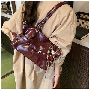 Détail du sac en cuir verni bordeaux avec sangles à boucles et charm décoratif