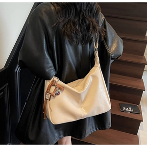 Détail d'un grand sac hobo en cuir crème avec un nœud tissé marron et charme en métal